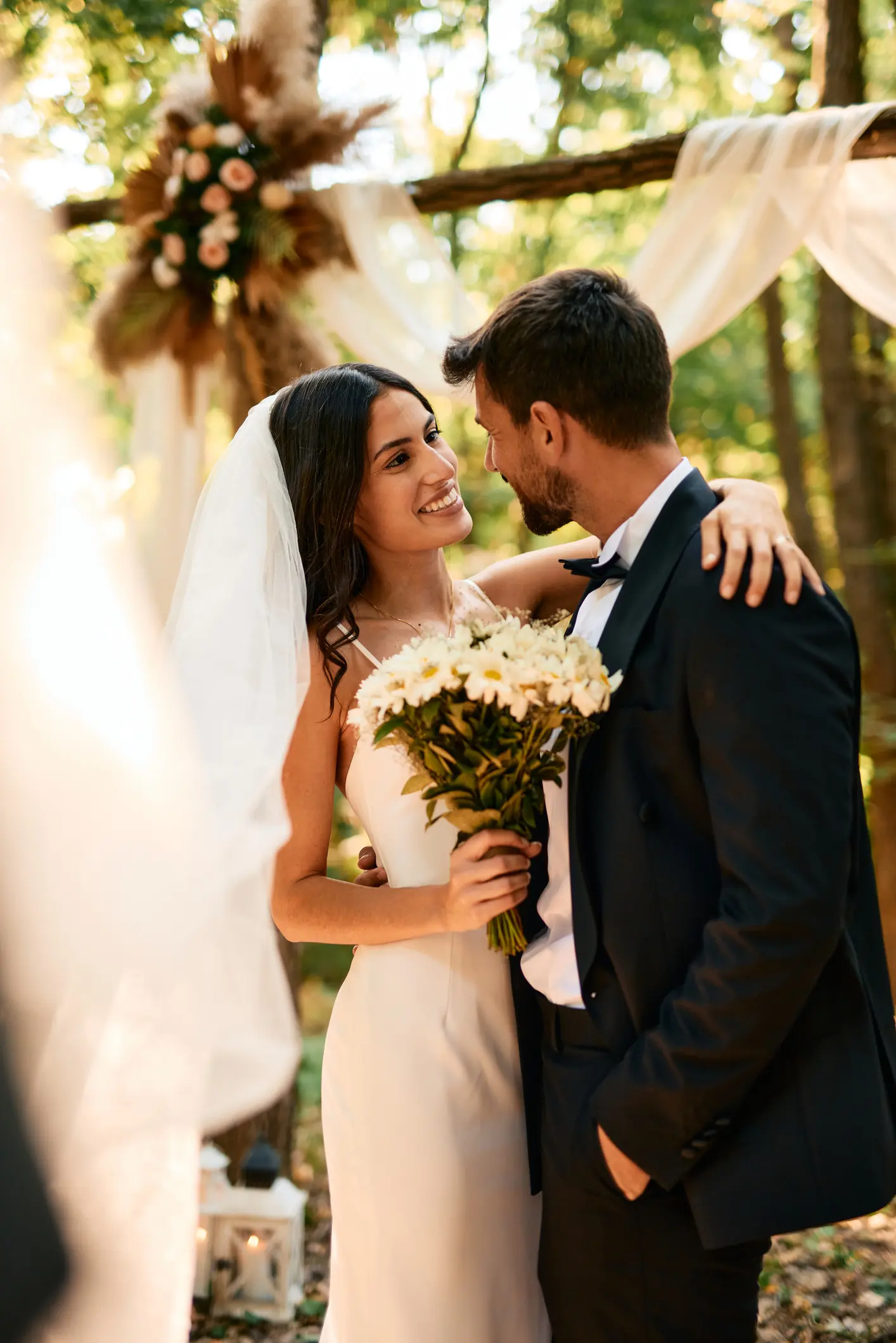 Bride and groom embracing and gazing into each other's eyes during their enchanting outdoor wedding ceremony in a serene forest, celebrating their love and commitment